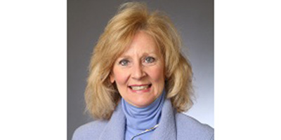 Portrait of a faculty member with shoulder-length blonde hair wearing a light blue jacket and turtleneck against a neutral background.
